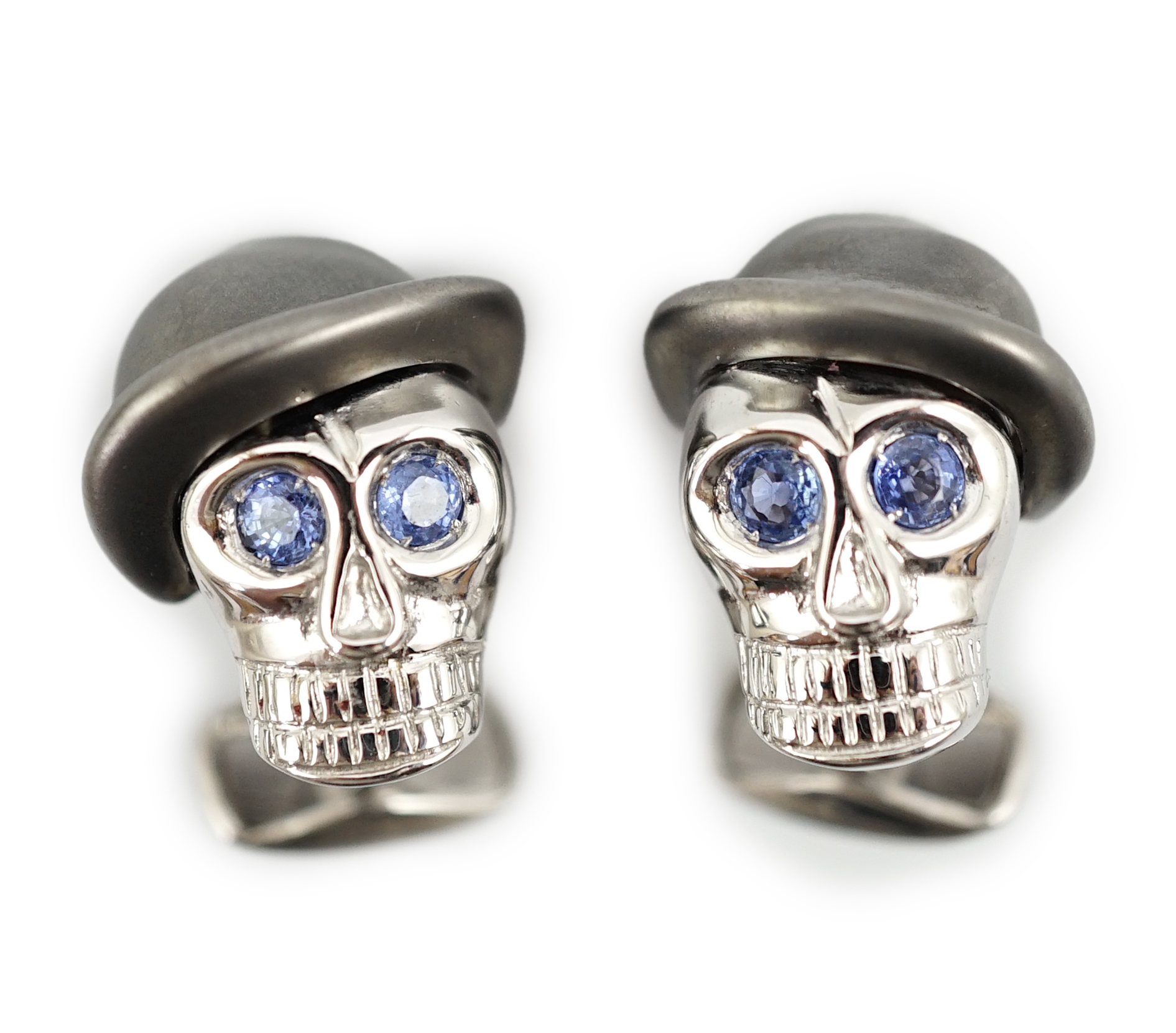 A modern pair of Longmire 18ct white gold, blackened rhodium and sapphire set novelty cufflinks, each modelled as a skull wearing a bowler hat